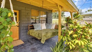 A cozy outdoor bedroom with a swing bed, stone walls, and lush greenery.