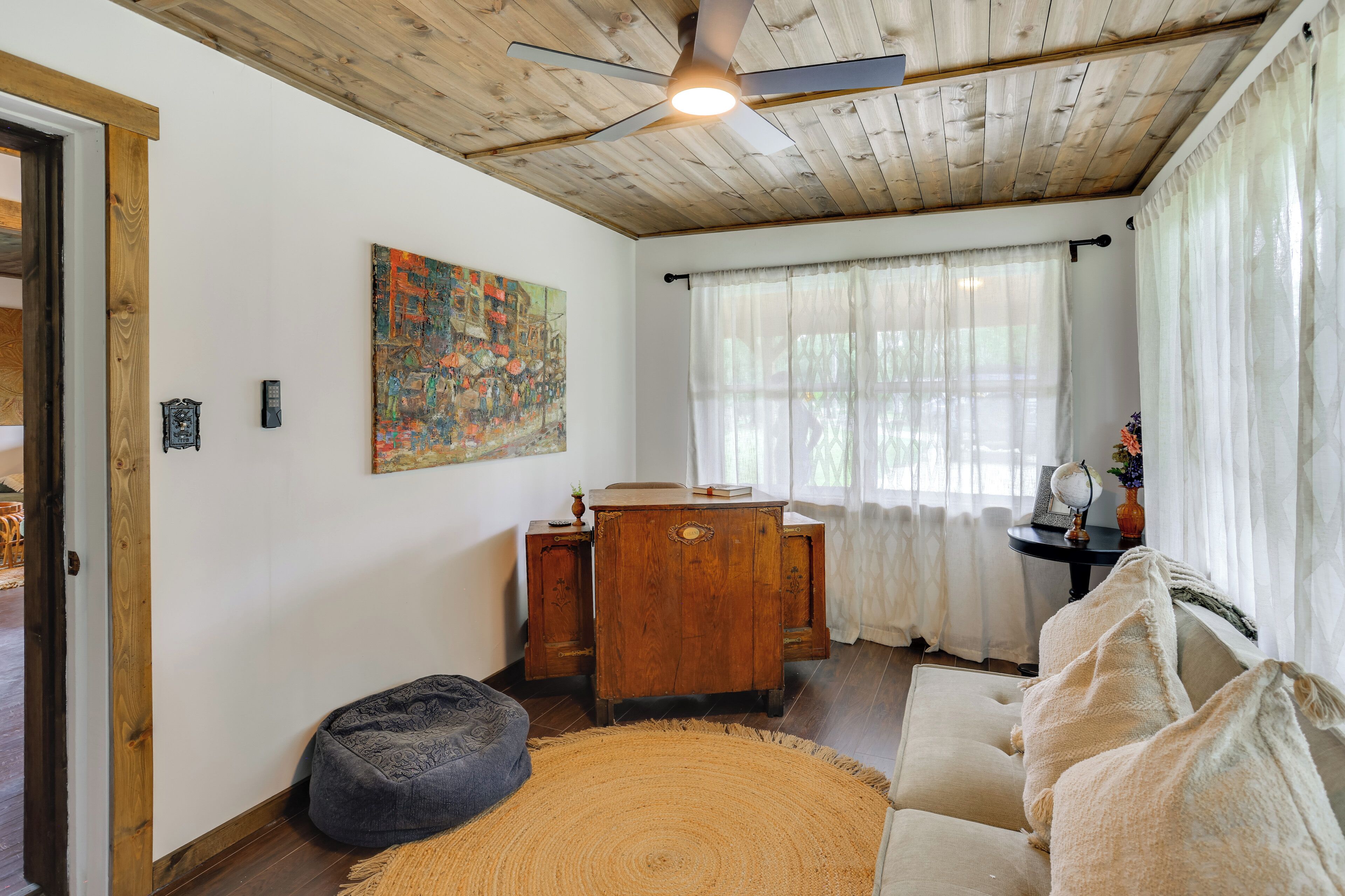A cozy room with a wooden ceiling, a round rug, a sofa, a desk, and a painting on the wall.