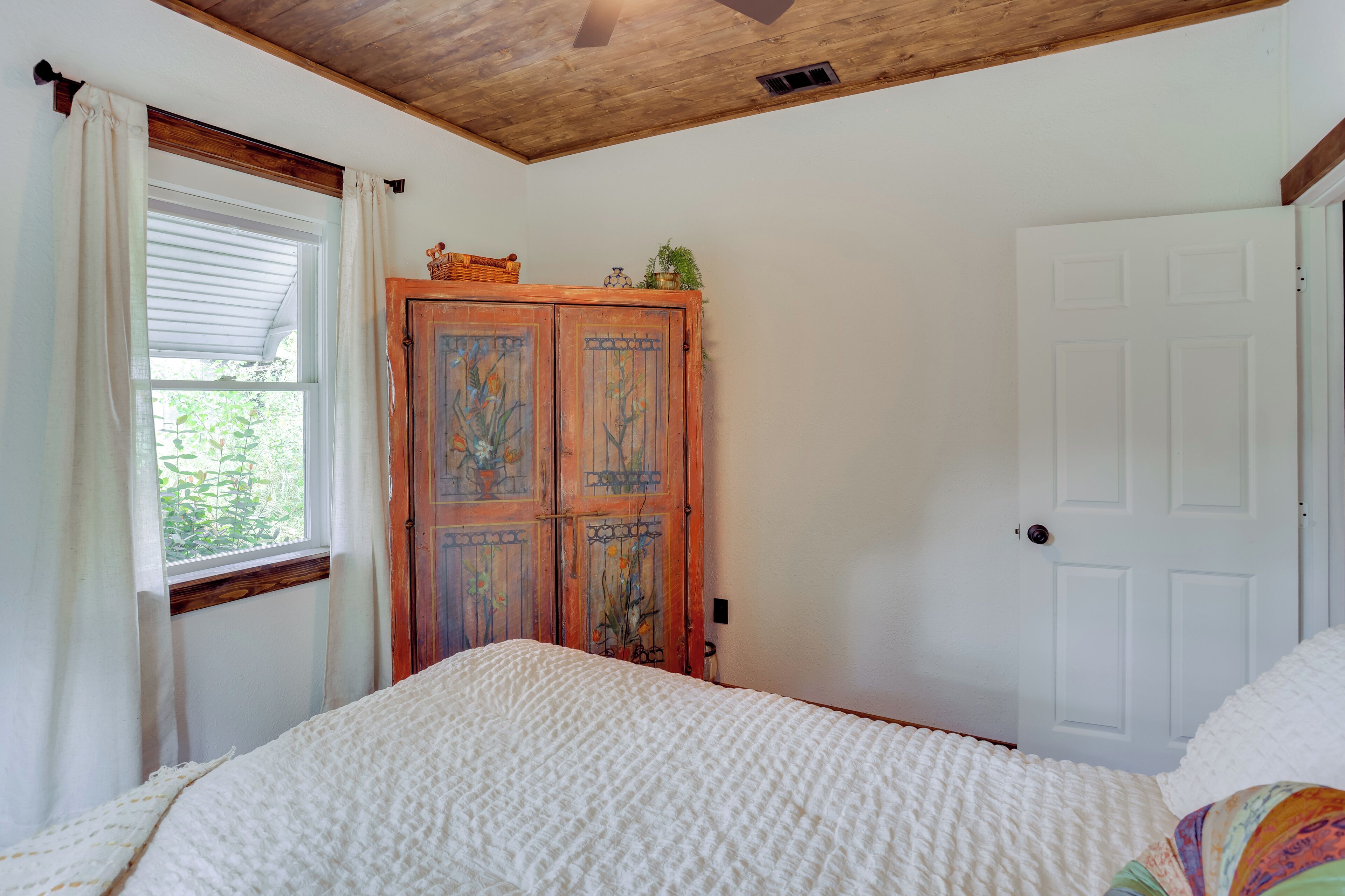 A bedroom with a wooden ceiling, a white door, and a window with curtains.