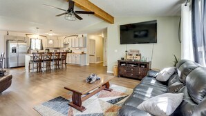 A spacious living room with a leather sofa, a wooden coffee table, and a large TV mounted on the wall. - Ozark Getaway Near Roaring River & Fishing (Cassville)