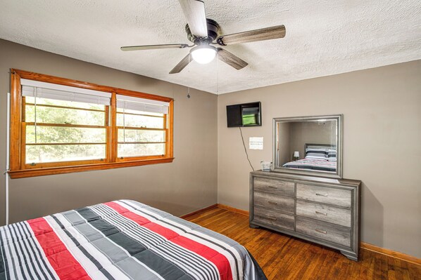 Une chambre à coucher comprenant un lit, une commode, un ventilateur de plafond, une fenêtre et un téléviseur.
