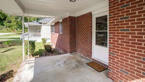 A covered porch with a brick exterior and a white door. - Walk to SC State University & Claflin: Cozy Home (Orangeburg)