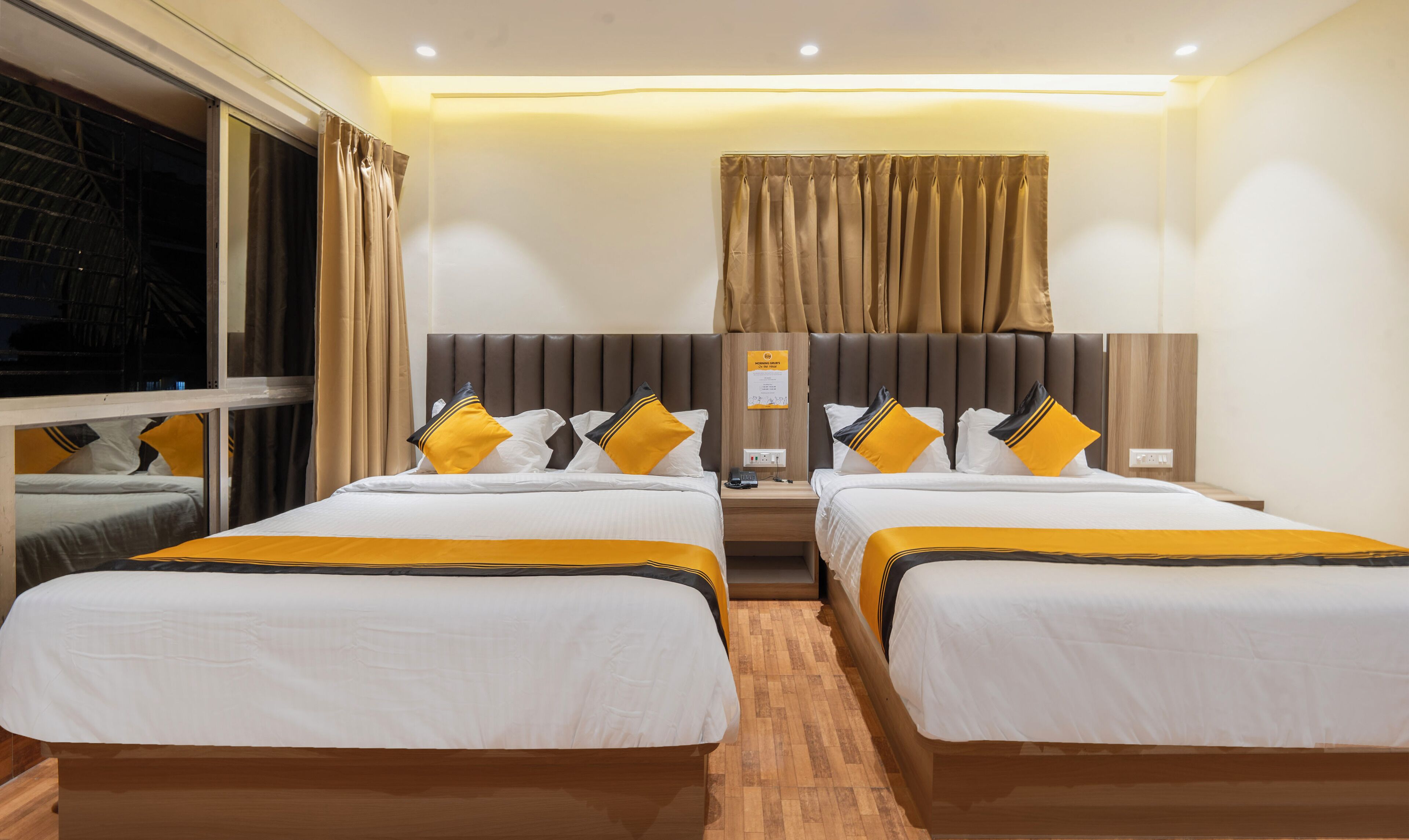 A hotel room with two beds, a wooden headboard, a nightstand, and a window with curtains.