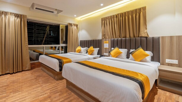 A hotel room with two beds, beige curtains, a wooden floor, and a wall-mounted air conditioner.