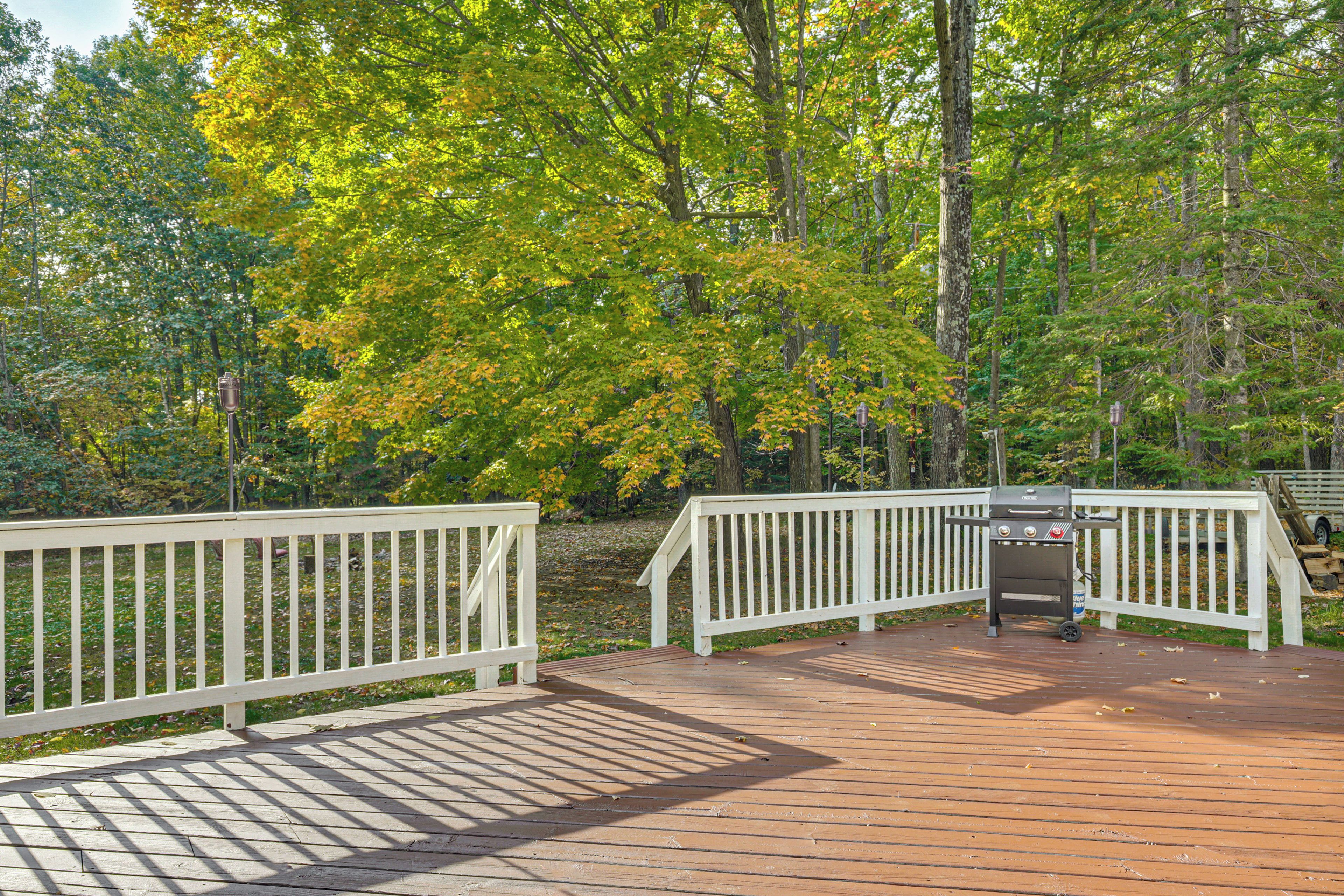 A wooden deck with white railings, surrounded by trees with green and yellow leaves.