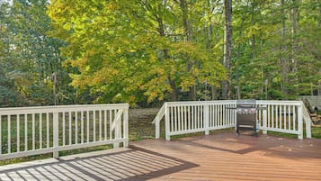 A wooden deck with white railings, surrounded by trees with green and yellow leaves.
