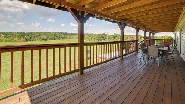 A covered porch with a wooden deck, a table with chairs, and a view of a green landscape. - Near Garden of the Gods: Home w/ Fire Pit, Hot Tub (Elizabethtown)