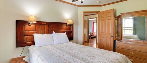 A bedroom with a large bed, wooden headboard, two bedside lamps, a ceiling fan, and a wooden dresser with a mirror.