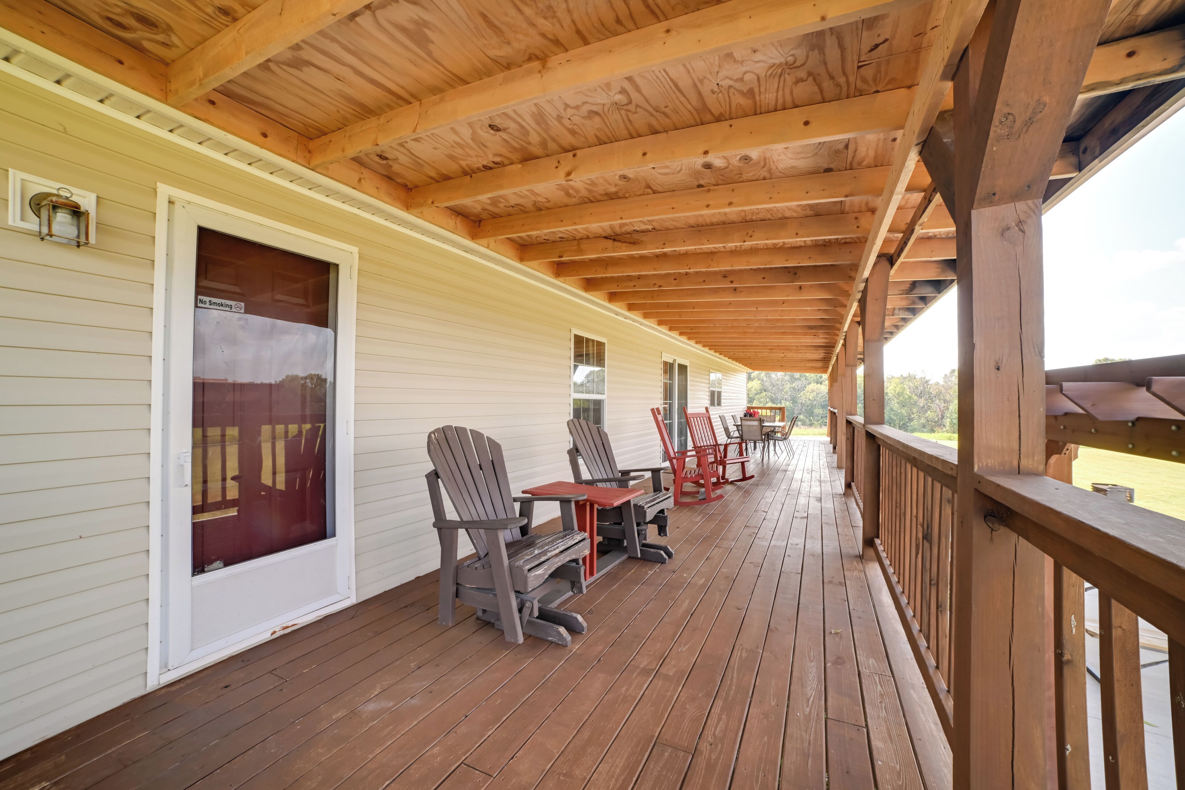 A covered porch with wooden beams, a sliding glass door, and outdoor seating with chairs and tables.