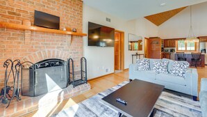 A modern living room with a brick fireplace, a flat-screen TV mounted above it, a light blue sofa with patterned cushions, and a wooden coffee table. - 3 Mi to Prettyboy Reservoir! Maryland Hideaway (Freeland)