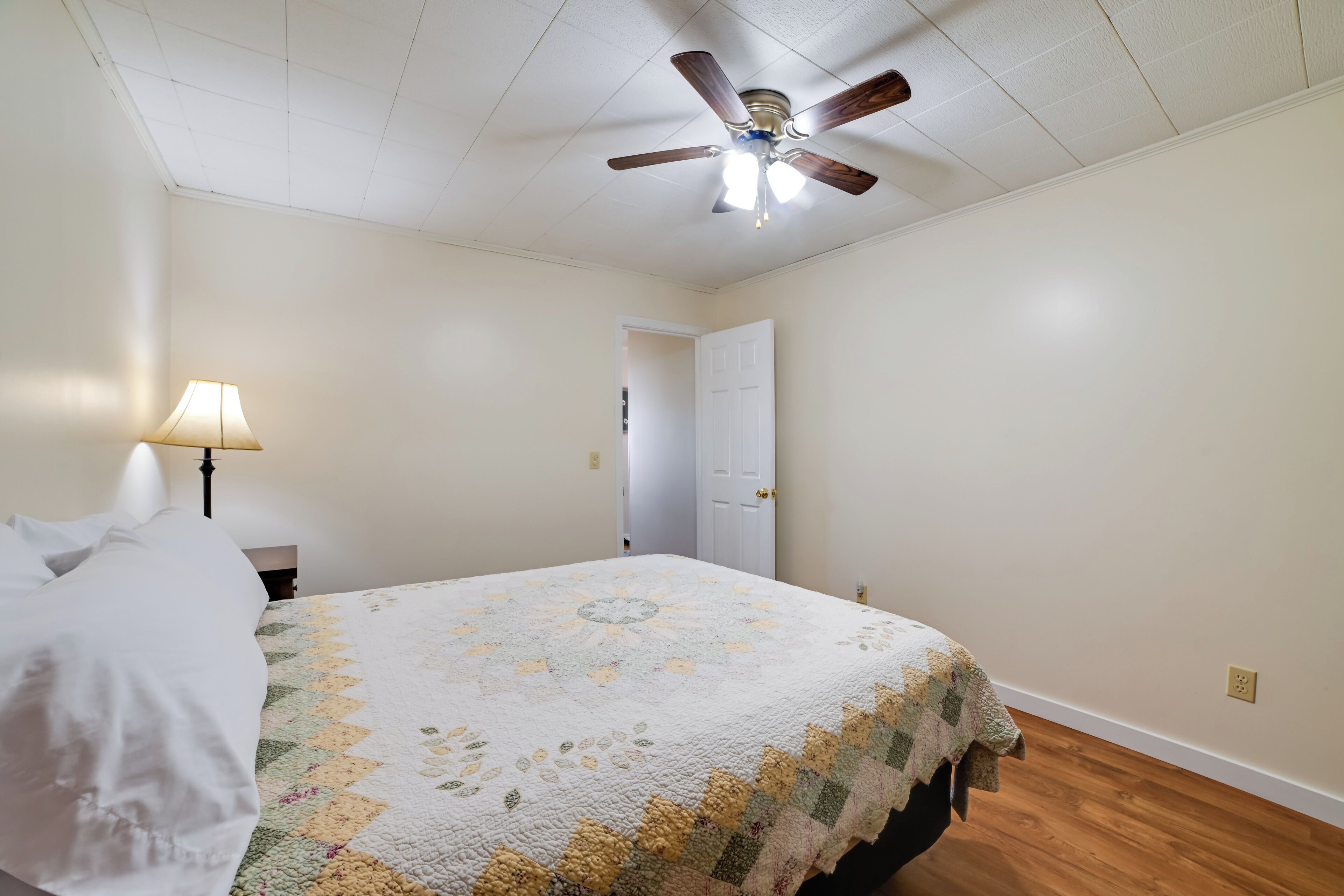 Quarto com cama, ventilador de teto, porta e abajur.