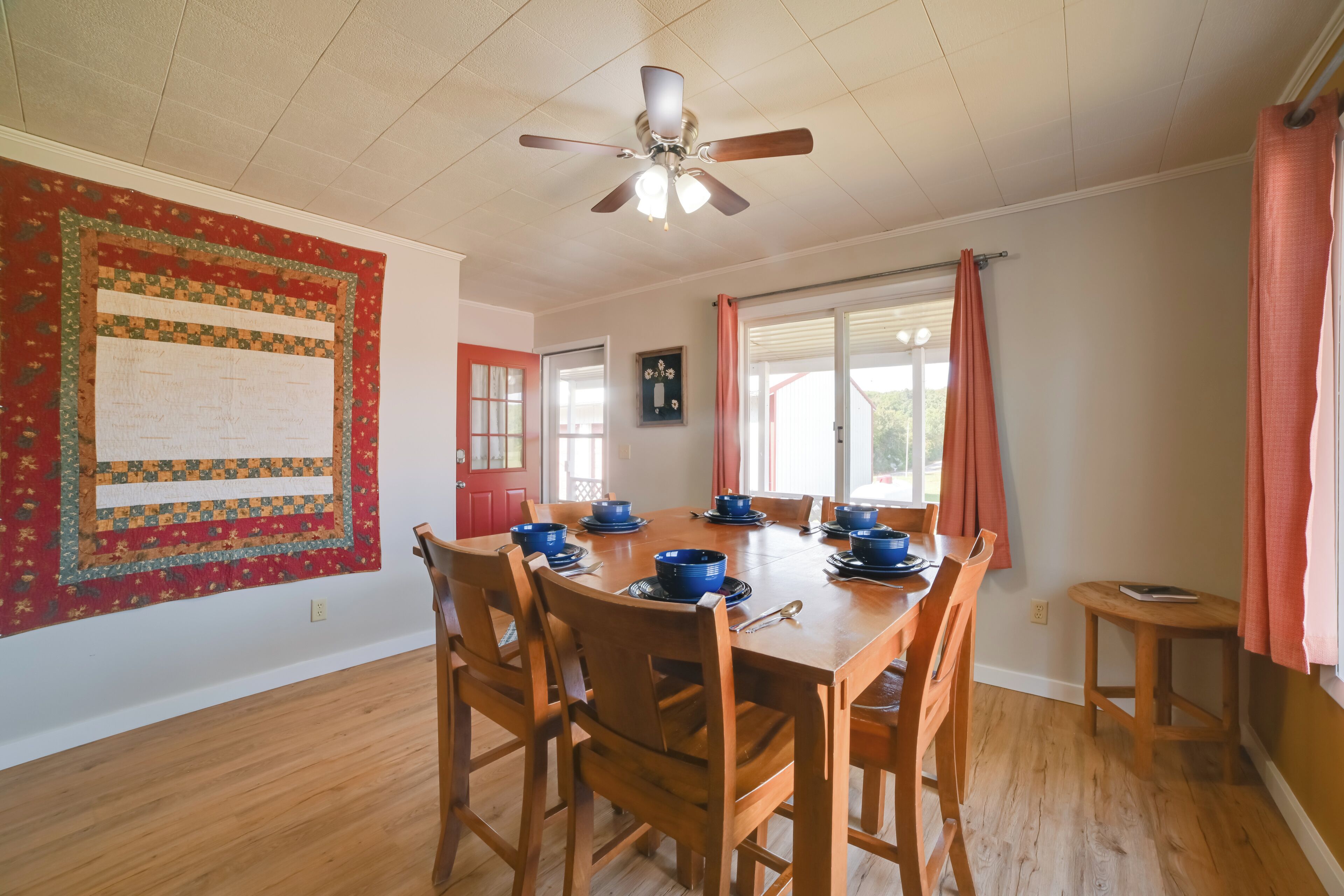 A dining area with a wooden table set for six, surrounded by wooden chairs. A ceiling fan is visible above the table.