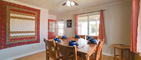 A dining area with a wooden table set for six, surrounded by wooden chairs. A ceiling fan is visible above the table.