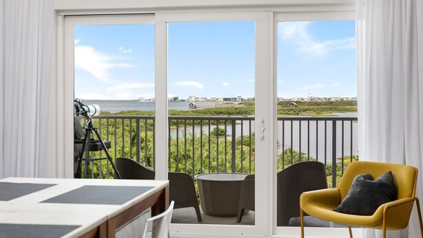 A balcony with a telescope, a table, and chairs, overlooking a body of water and buildings. - Las Velas Village Luxury with a view (South Padre Island)