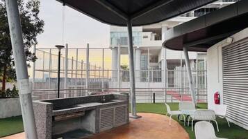 An outdoor patio with a stone sink, white chairs, and a view of a modern building.