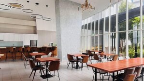 A modern cafe with wooden tables and chairs, large windows, and a kitchen area. - Encorp Marina Residences Puteri Habour (Iskandar Puteri)