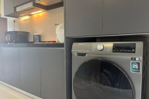 Une cuisine moderne et compacte, dotée d’un lave-linge et d’un sèche-linge intégrés, d’un four à micro-ondes et d’une machine à café posée sur le plan de travail.