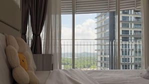 A hotel room with a bed, a large window with a view of a cityscape, and a teddy bear on the bed. - Encorp Marina Residences Puteri Habour (Iskandar Puteri)