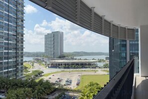 Une vue depuis un balcon donnant sur un parking, un immeuble et une étendue d’eau.