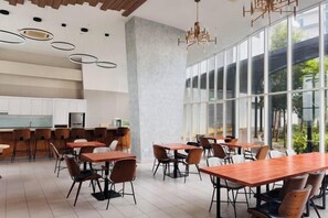 Un espace de restauration moderne avec des tables et des chaises, de grandes fenêtres et une cuisine en arrière-plan.