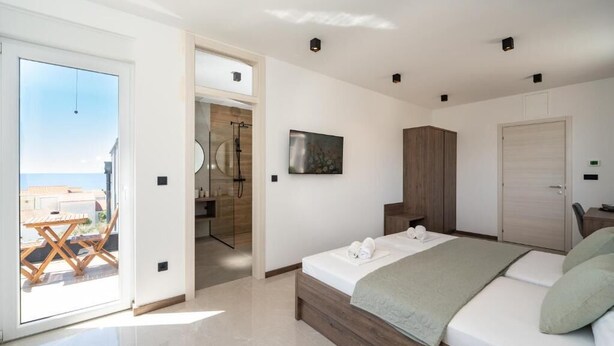 A modern bedroom with a bed, a wooden wardrobe, a bathroom with a shower, and a view of the sea through a glass door. - The old man and the sea Inn-Double room with balcony and Sea view (Novalja)