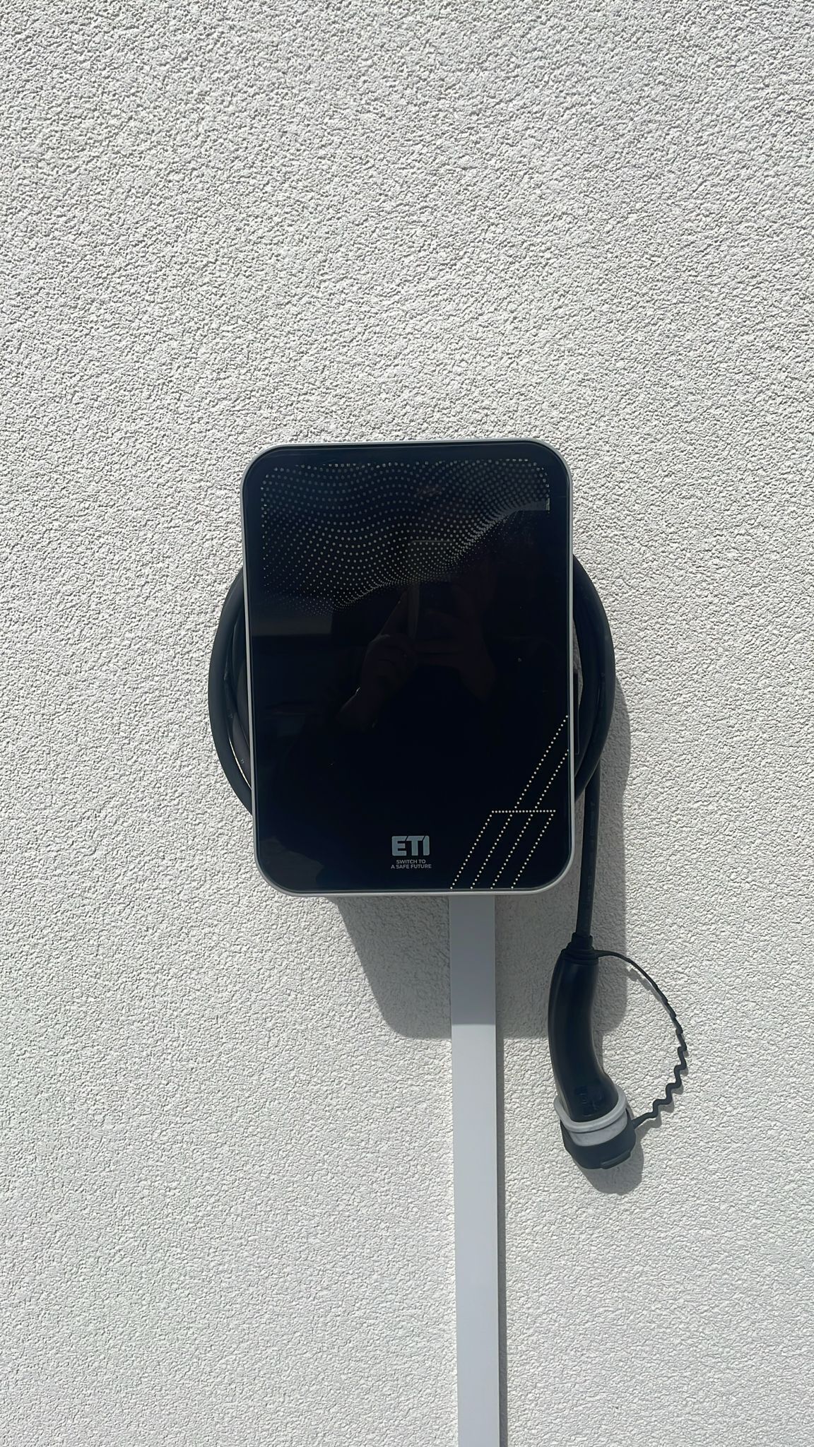 A black device with a white cord, mounted on a textured wall.