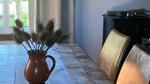 Un tavolo da pranzo con tovaglia tessuta, un vaso di ceramica marrone con fiori secchi e due poltrone in pelle.