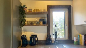 Una cucina compatta con lavello integrato, due macchine da caffè, una finestra con vista sul verde e mensole con barattoli e tazze.