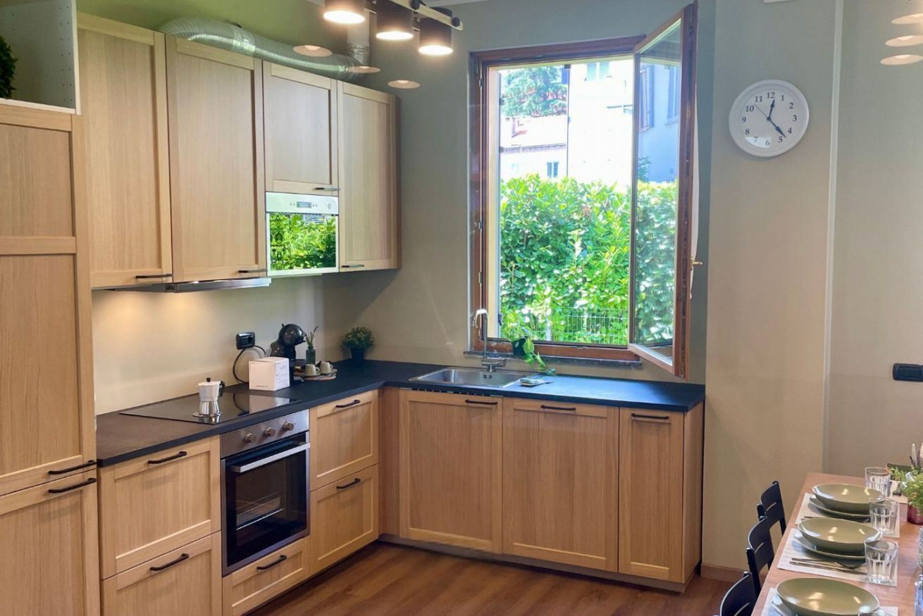 A modern kitchen with wooden cabinets, a built-in oven, and a window with a view of greenery.