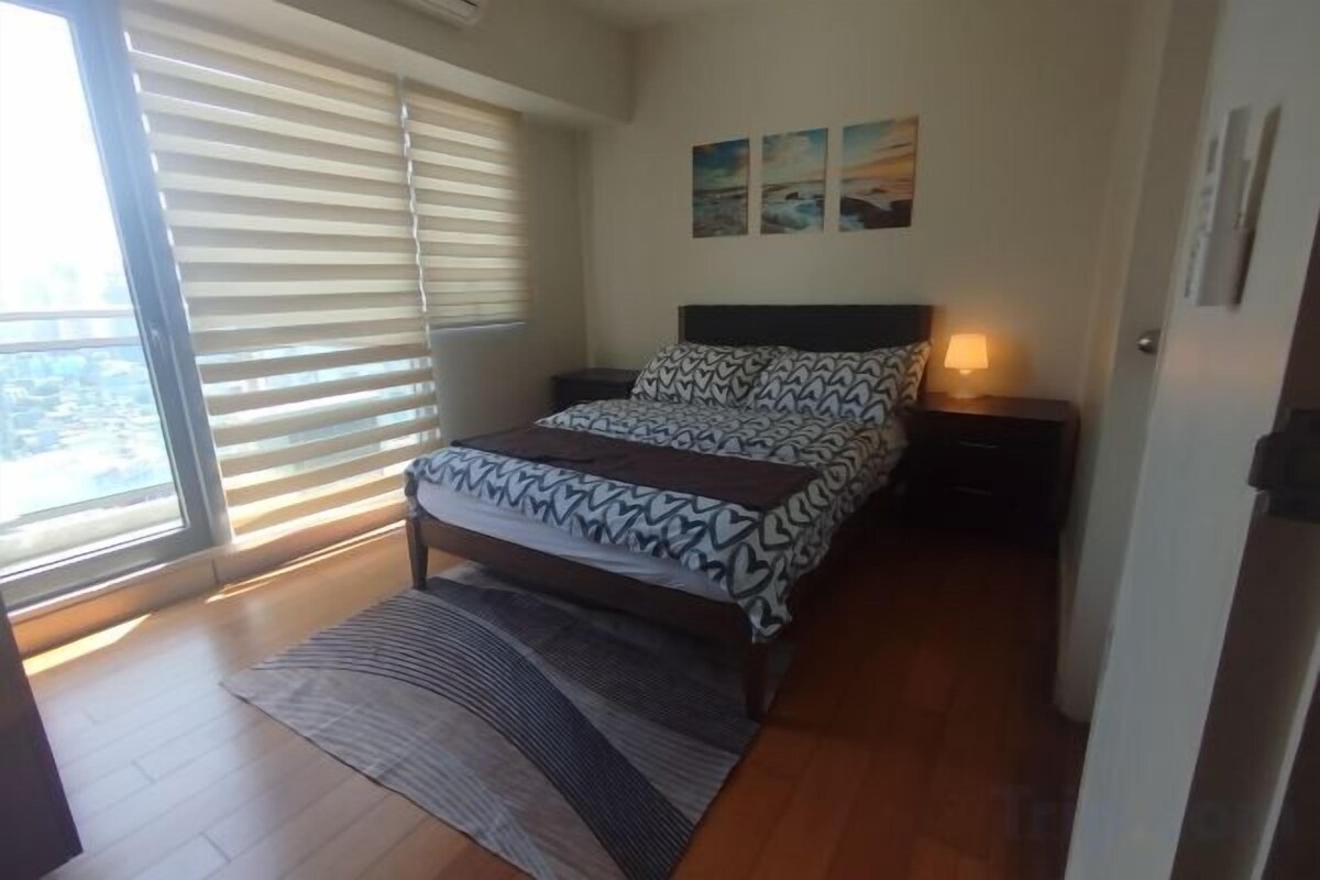 Une chambre à coucher avec un lit, une table de chevet, une lampe et une fenêtre avec des stores.