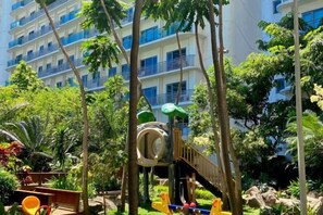 A playground with slides and climbing structures surrounded by trees and greenery. - Aveline Suites II, Garden/City view,2br, amenities (Mandaluyong)