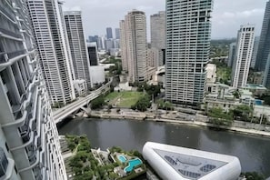 A high-rise building with a river in the foreground and other high-rise buildings in the background. - Aveline Suites II, Garden/City view,2br, amenities (Mandaluyong)