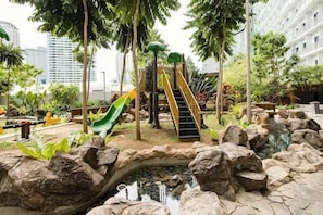 A playground with slides and stairs, surrounded by rocks and plants.