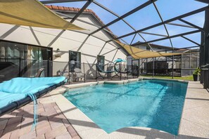 A swimming pool with a sunshade, lounge chairs, and a covered patio area.