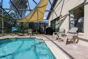 Ein Poolbereich mit Glasveranda, Sitzgelegenheiten im Freien und einem schattigen Platz.