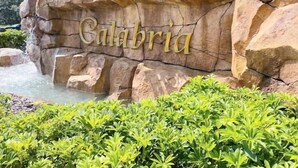 Un mur de pierres sur lequel est gravé le mot « Calabre », entouré d’une végétation luxuriante et agrémenté d’une petite cascade.