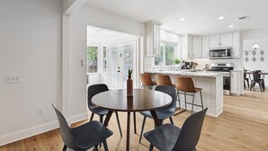 A modern kitchen with white cabinetry, a central island, and a dining area with a round table and chairs.
