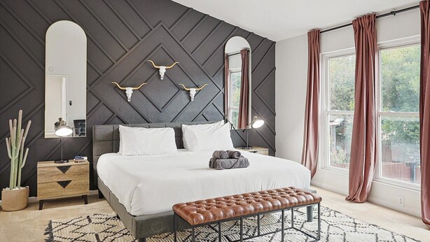 A modern bedroom with a bed, bedside tables, a bench, a large mirror, and decorative wall elements.