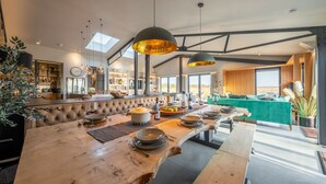 A modern kitchen with a long wooden island, pendant lighting, and a view to the dining area. - Indigo Barn, Warham, Norfolk (Warham)