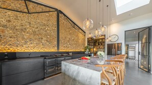 A modern kitchen with a stone backsplash, a marble island, wooden chairs, and pendant lighting. - Indigo Barn, Warham, Norfolk (Warham)