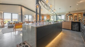 A spacious living area with a large island, modern kitchen, and large windows offering a view of the outdoors. - Indigo Barn, Warham, Norfolk (Warham)