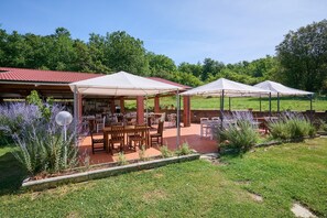 A covered outdoor seating area with tables and chairs, surrounded by greenery and trees. - Room 'Santa Lorica - Camera 12' with Shared Pool, Shared Garden and Wi-Fi (Sassetta)