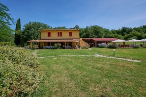 A two-story yellow building with a red roof, surrounded by a grassy lawn and trees.