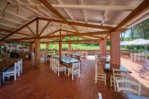 An outdoor covered patio with wooden tables and chairs, brick pillars, and a view of a green landscape. - Room 'Santa Lorica - Camera 12' with Shared Pool, Shared Garden and Wi-Fi (Sassetta)