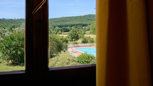 A view through a window of a swimming pool surrounded by trees and hills. - Room 'Santa Lorica - Camera 13' with Shared Pool, Wi-Fi and Air Conditioning (Sassetta)