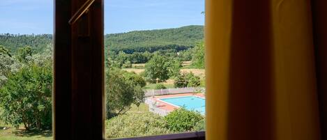 A view through a window of a swimming pool surrounded by trees and hills.