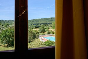 A view through a window of a swimming pool surrounded by trees and hills. - Room 'Santa Lorica - Camera 13' with Shared Pool, Wi-Fi and Air Conditioning (Sassetta)