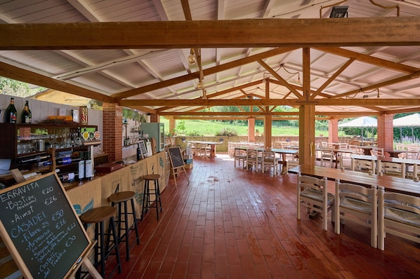 An outdoor café with wooden tables and chairs, a bar area with bottles and glasses, and a chalkboard menu. - Room 'Santa Lorica - Camera 13' with Shared Pool, Wi-Fi and Air Conditioning (Sassetta)