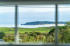 A coastal landscape with a grassy hill, a beach, and a cliff. - The Granary - 2 Bedroom Cottage - Penally (Tenby)