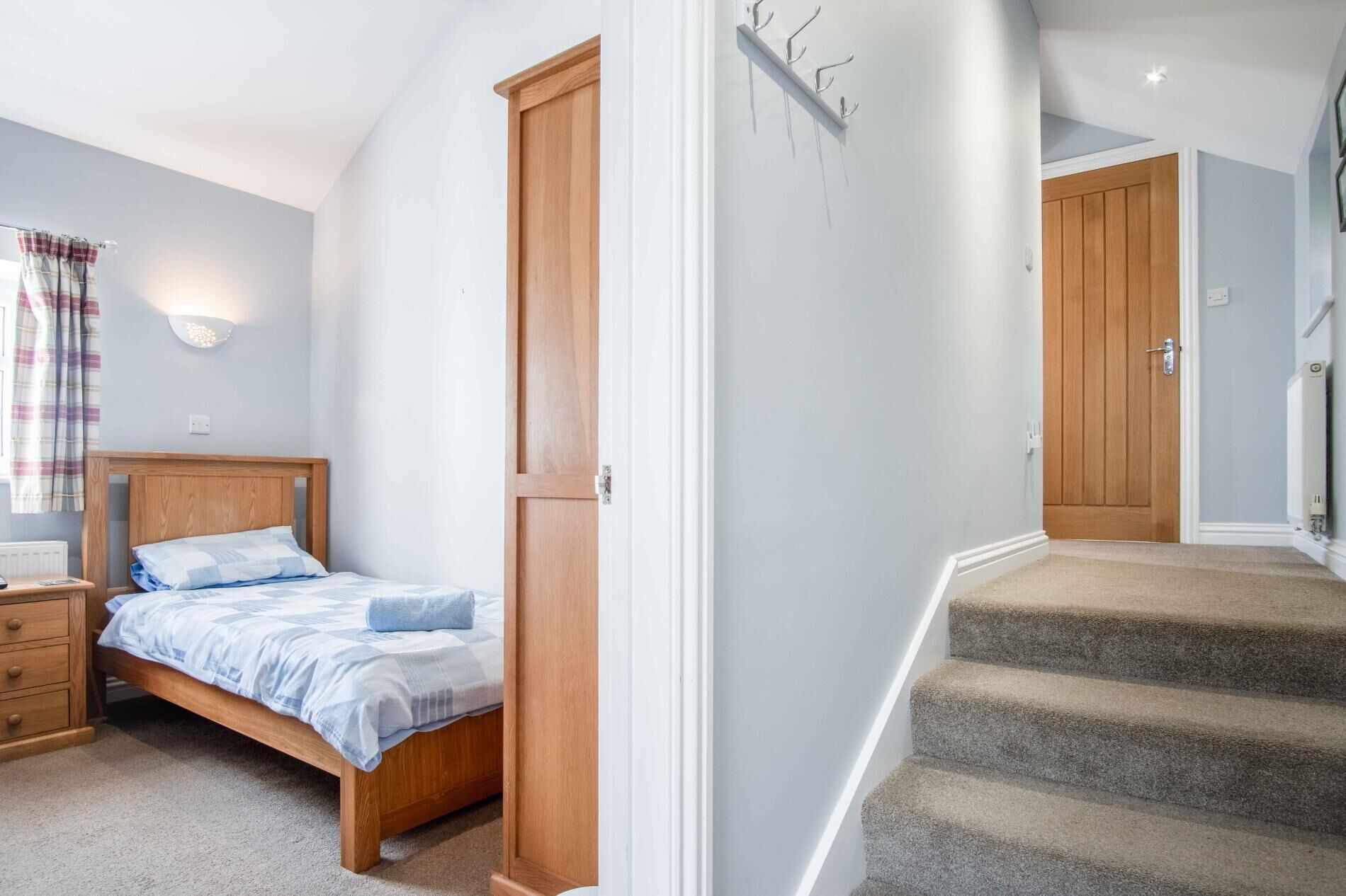 A bedroom with a wooden bed, a nightstand, a dresser, and a staircase leading to another room.